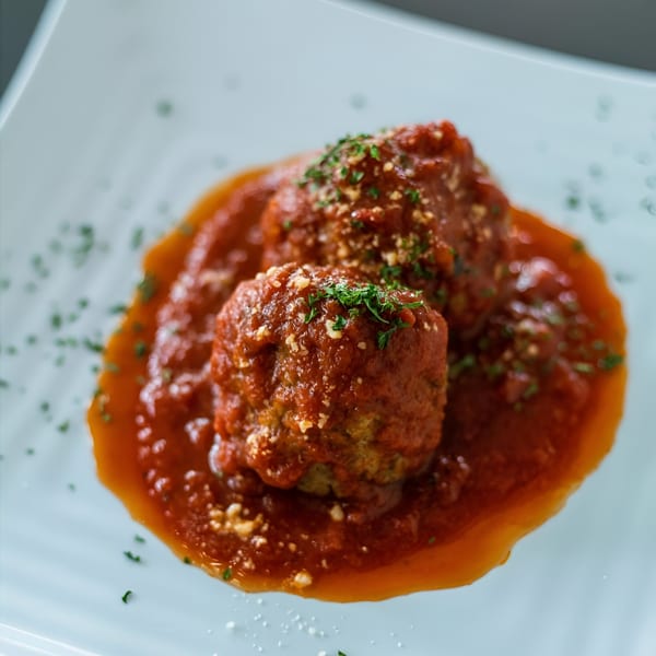 Two meatballs covered in red sauce, parmesan cheese, and parsley on a white plate.
