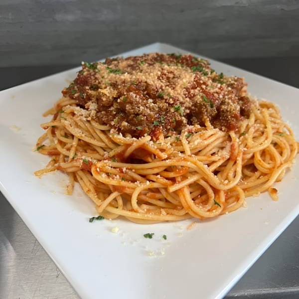 Spaghetti with meat sauce, parmesan cheese, and parsley on a white square plate.