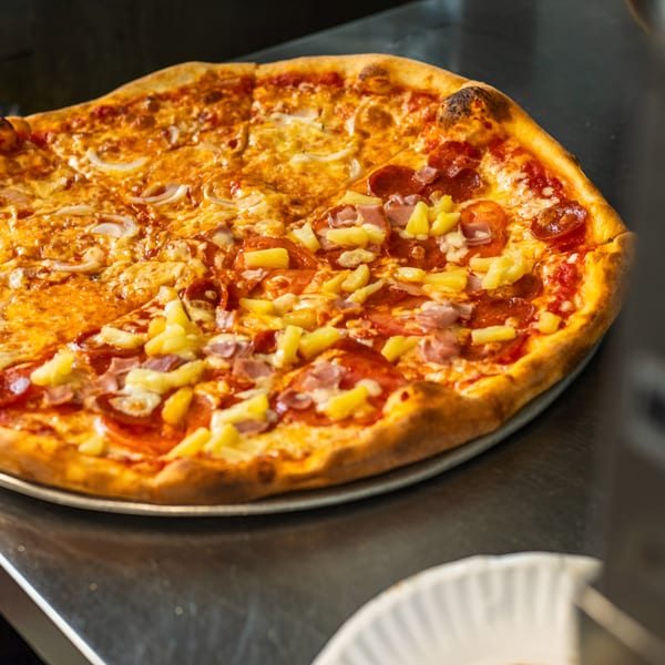 Vittorio's Pizza with half onion and half pepperoni, ham, and pineapple toppings on a metal counter.