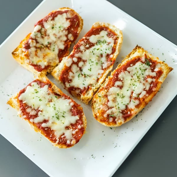 Four slices of Vittorio's Pizza garlic bread with melted cheese and red sauce on a white plate.