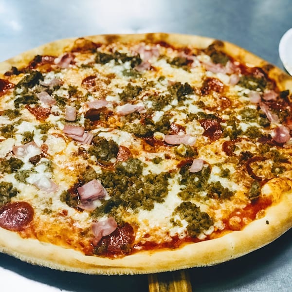 A whole Vittorio's Pizza with pepperoni, sausage, ham, and ricotta cheese on a metal surface.