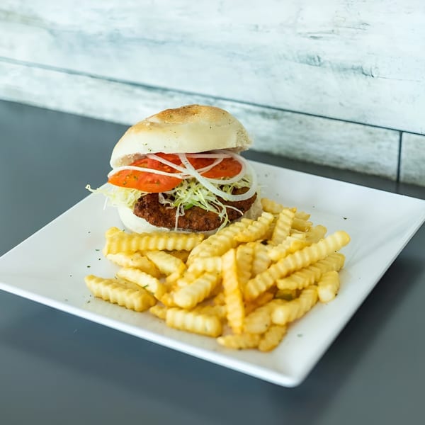 Vittorio's Pizza burger with lettuce, tomato, and onion, served with crinkle-cut fries on a white plate.