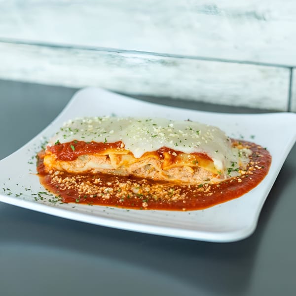 Vittorio's Pizza lasagna, with layers of pasta, meat, cheese, and red sauce, garnished with parsley.